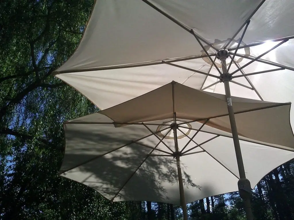 Twee grote witte parasols die op een zonnige dag een zandstrand in de schaduw stellen in Enschede